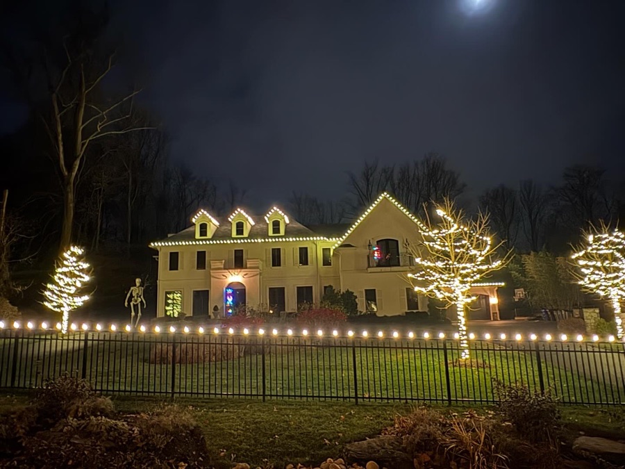 Large estate home with roofline lighting and wrapped trees flanking the entry