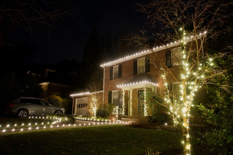 Brick colonial with roofline lighting and a lit pathway along the driveway