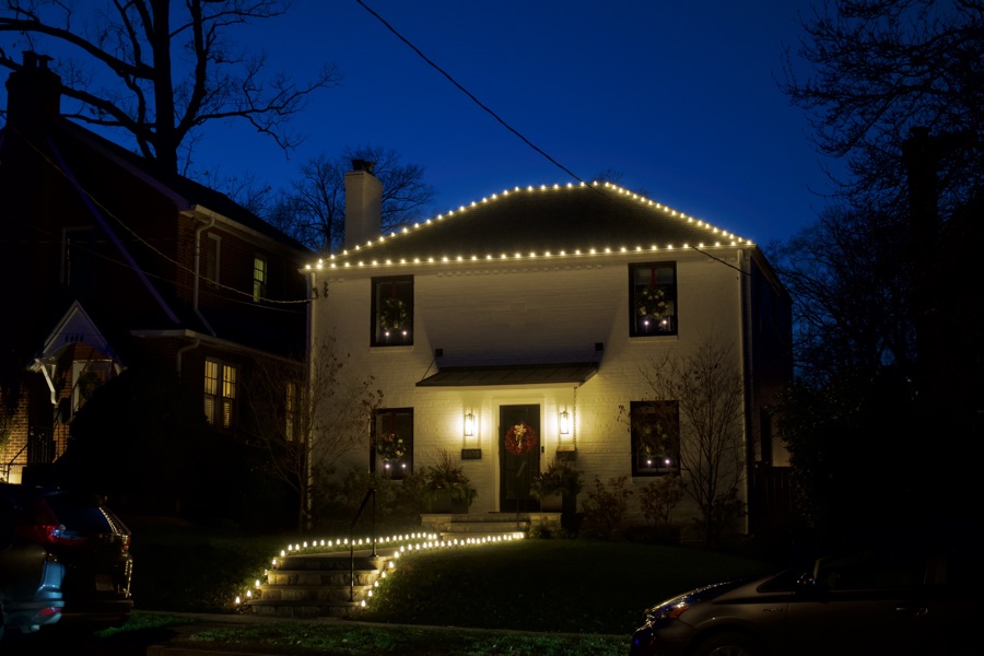 White colonial home with roofline lighting and a lit walkway to the front door