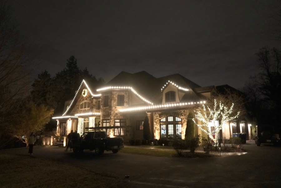 Large stone and stucco estate with roofline lighting and wrapped trees