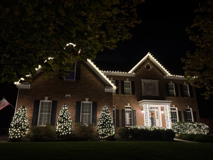 Brick colonial home with roofline lighting and wrapped trees