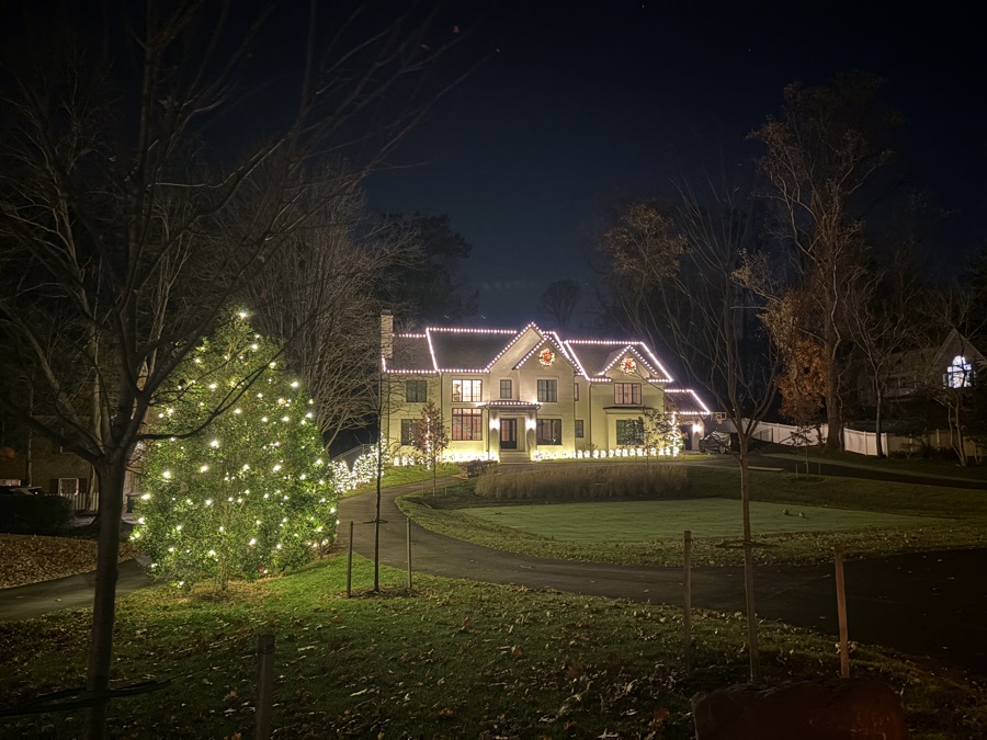 Farmhouse-style home with a large fully lit conifer tree in the yard