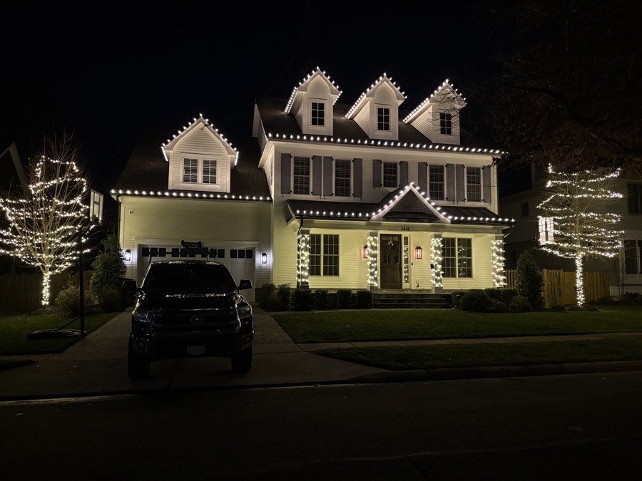 Colonial home with multiple dormers, roofline lighting, and trees wrapped on both sides