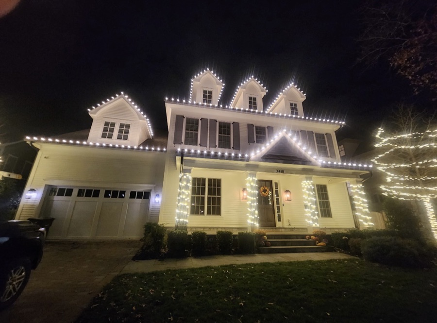 White colonial home with dormer and roofline lighting and lit entry columns