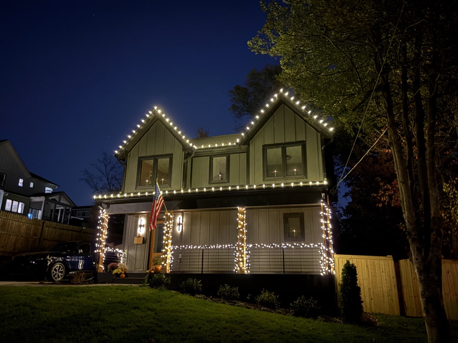Green modern farmhouse with roofline, column, and porch railing lighting at dusk