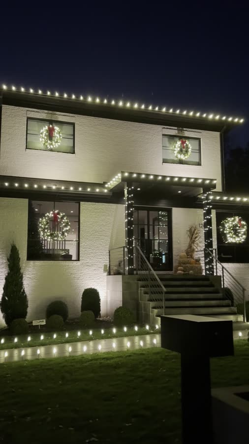 Brick colonial with roofline lighting and wreaths in the upstairs windows