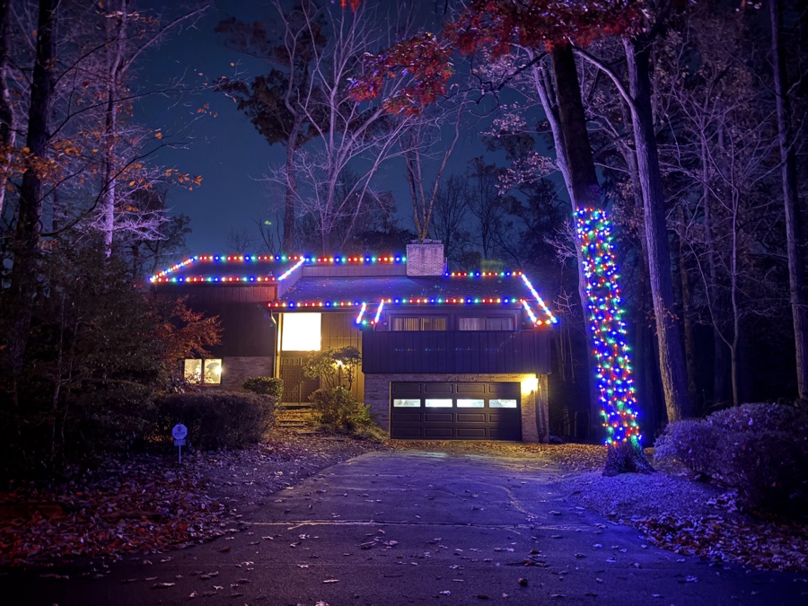 Wooded home with multicolor roofline lighting and a wrapped tree