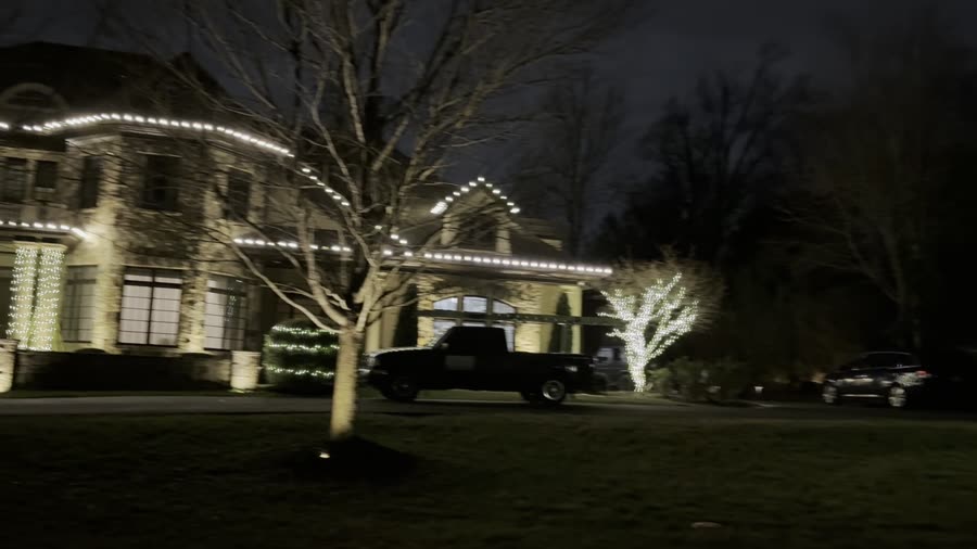 Stone estate with roofline lighting and wrapped trees along the driveway