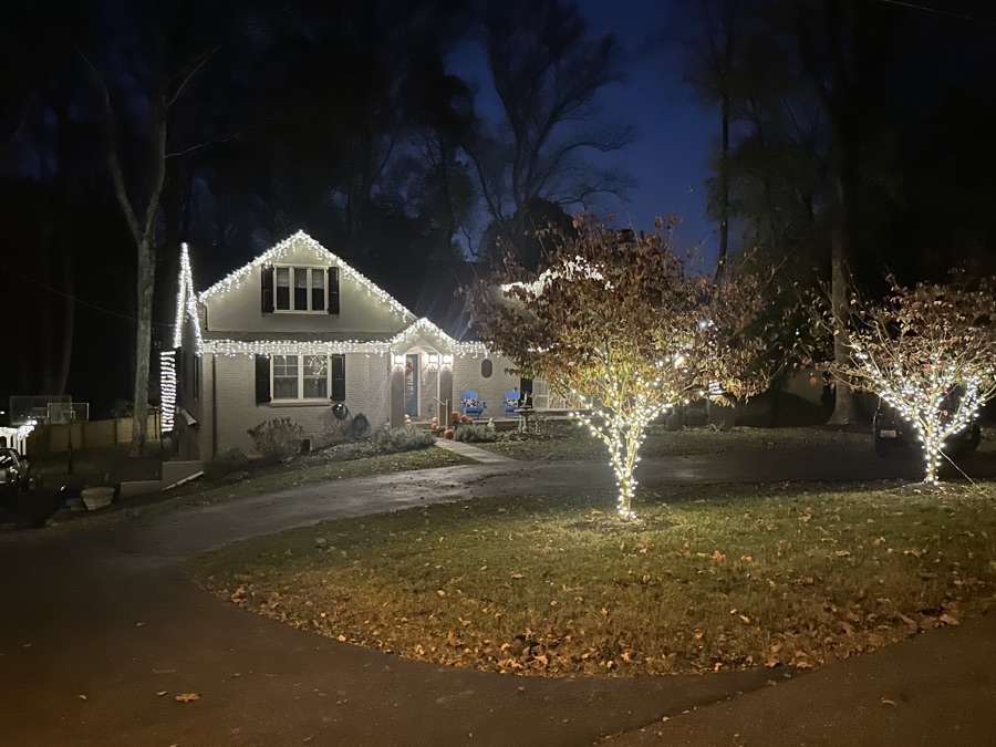 Cottage-style home with icicle roofline lighting and two wrapped lawn trees