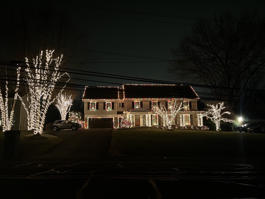 Brick colonial viewed from the street with roofline lighting and multiple wrapped trees