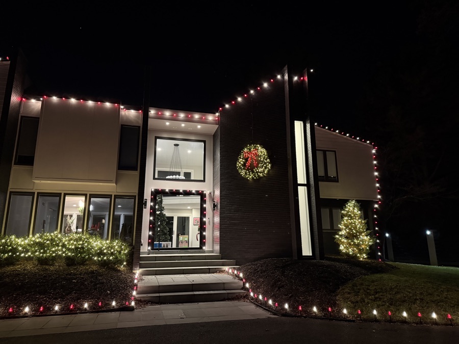 Modern home with red and white roofline lighting and a wreath at the entry