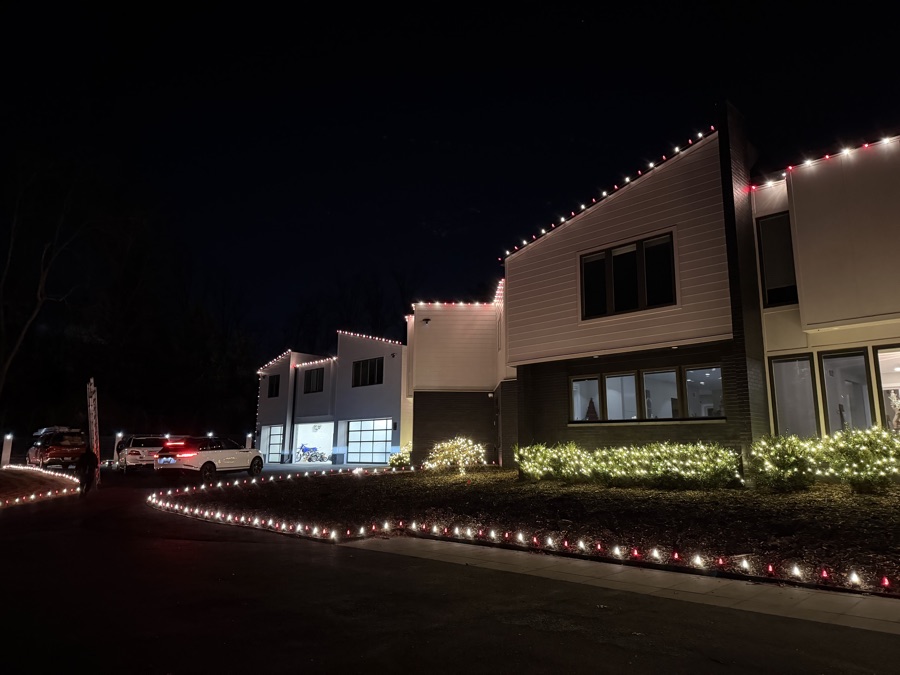 Modern home with roofline lighting and red and white lights along the driveway edge