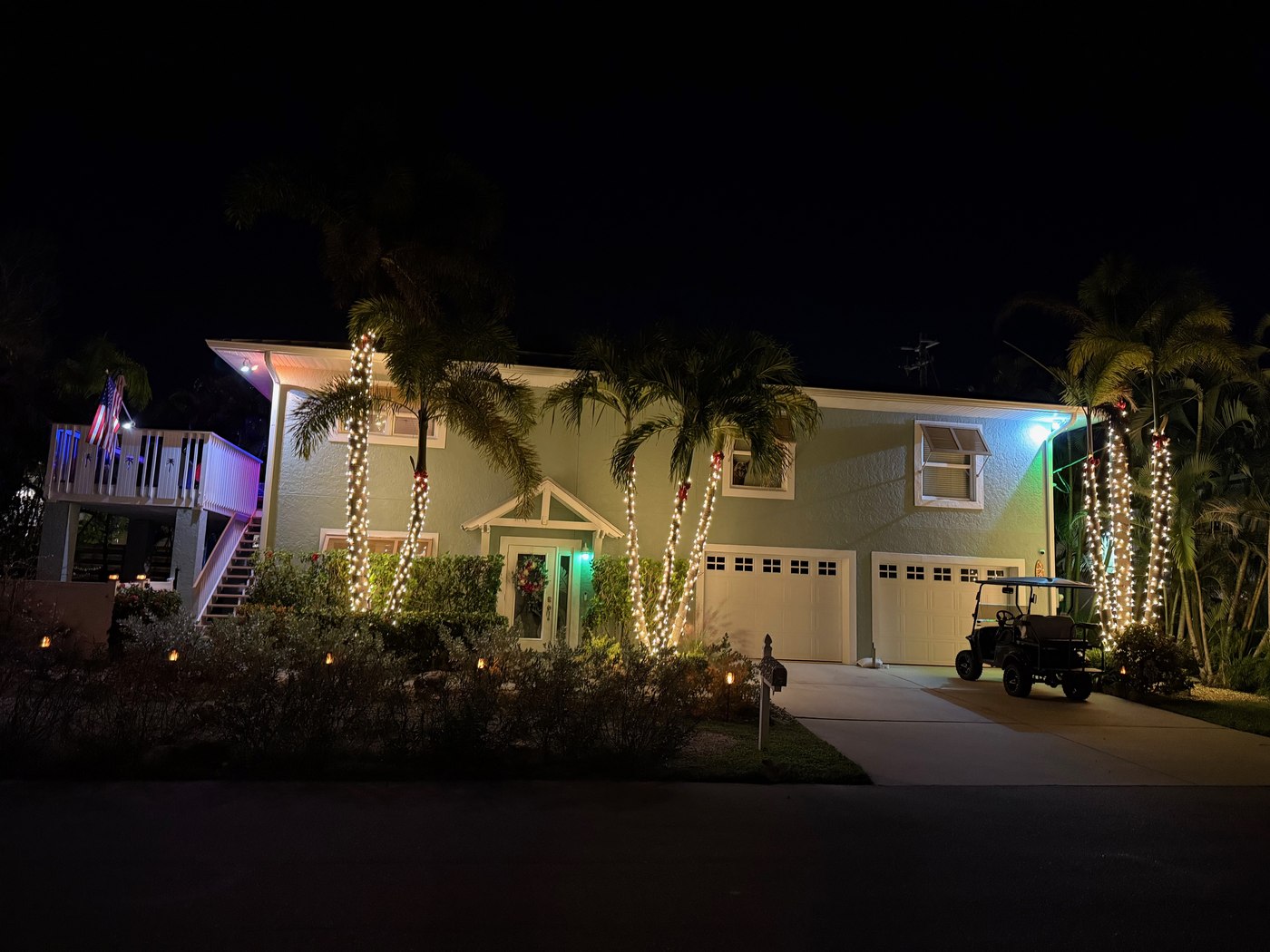 Elevated island home with wrapped palms flanking the entrance and garage, a golf cart parked in the driveway, at night on Anna Maria Island