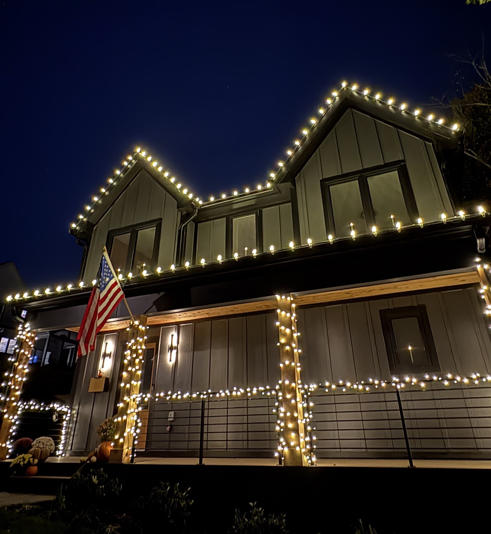 Full two-story home lit with warm white roofline lighting along both gables and wrapped porch posts at dusk